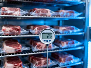 Soczysty stek wołowy medium-rare z rozpuszczonym masłem ziołowym na drewnianej desce, otoczony świeżymi ziołami i czosnkiem.